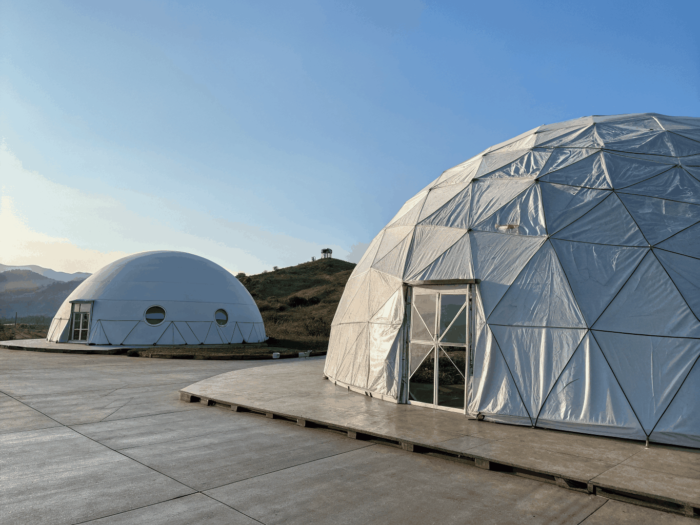 Illuminated geodesic dome tent in desert terrain at dusk